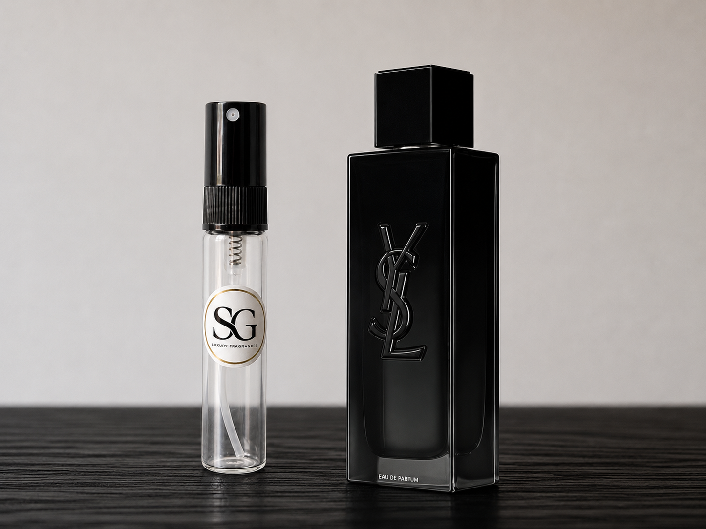 Black perfume bottle and smaller spray bottle on a wooden surface with a neutral background