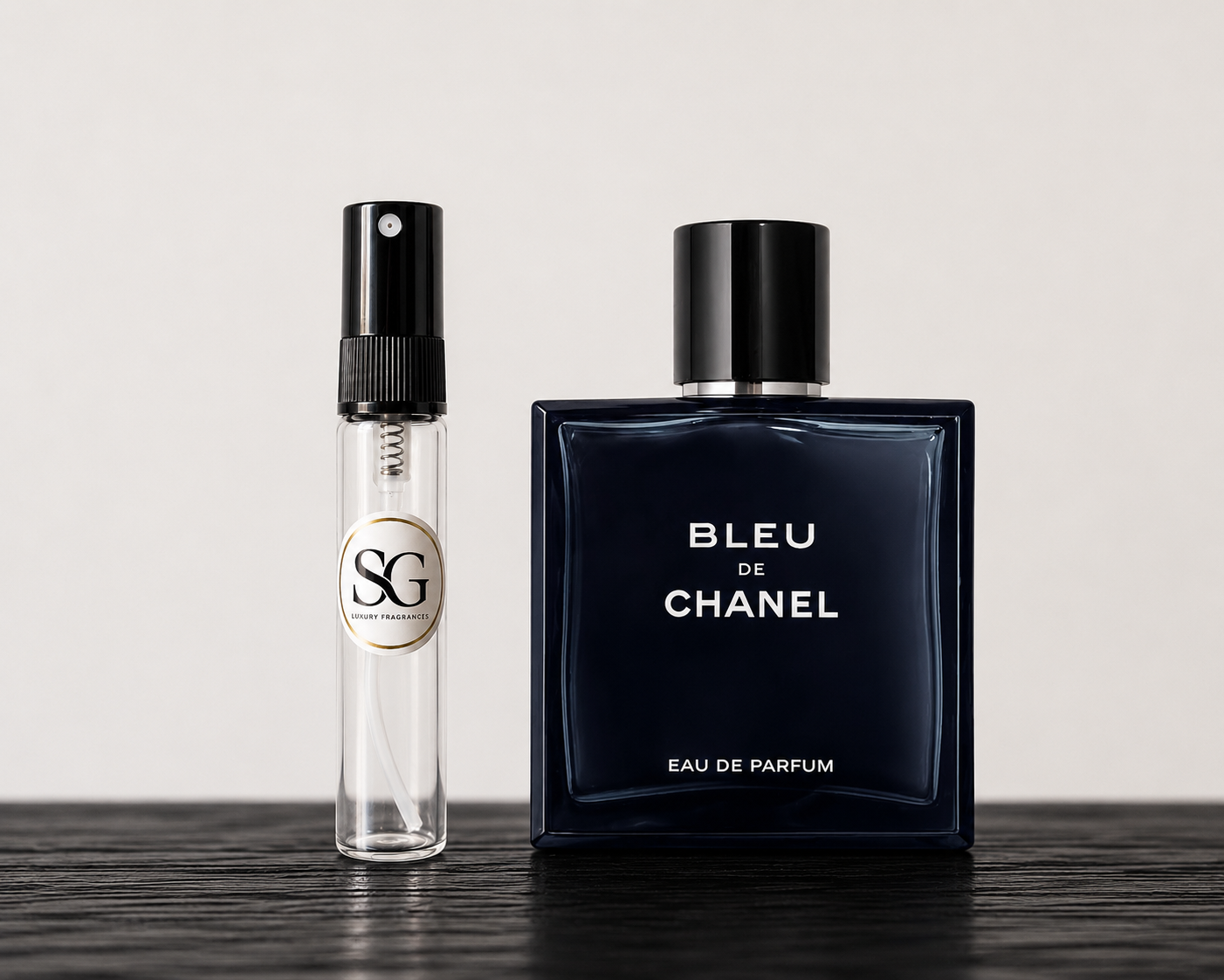 Bleu de Chanel perfume bottle and a smaller clear bottle with black cap on a wooden surface.