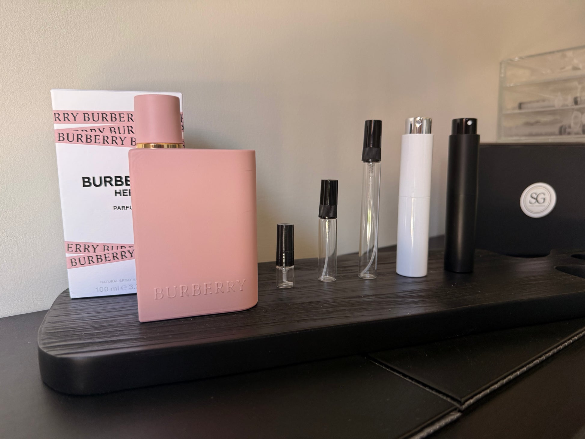 Pink Burberry perfume bottle on a wooden surface with other small bottles and packaging.