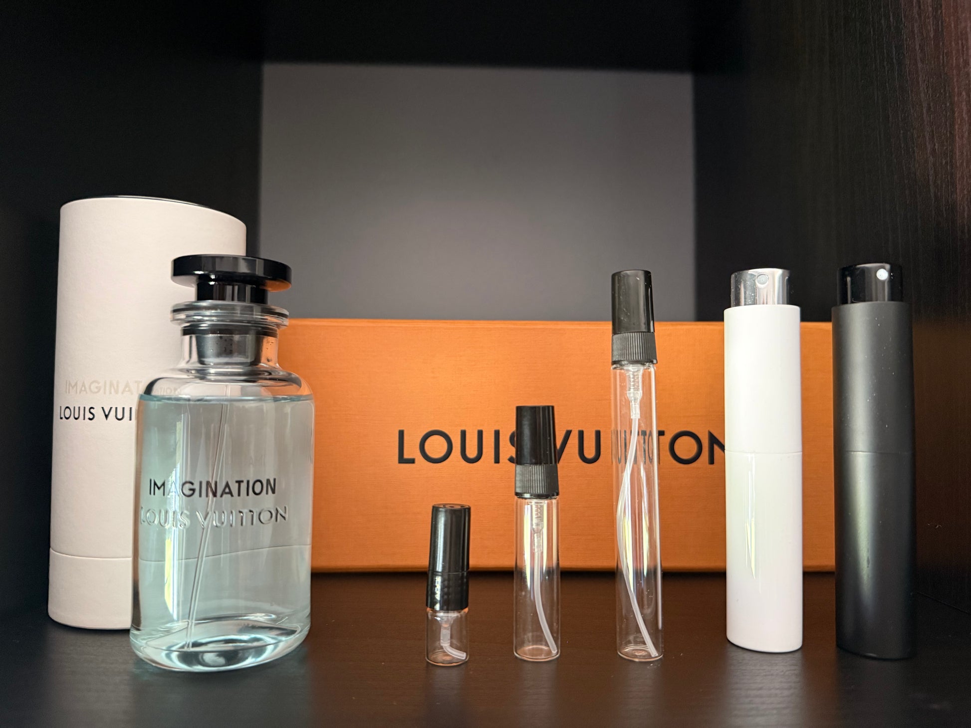 Louis Vuitton perfume bottles and packaging on a dark surface with an orange box in the background.