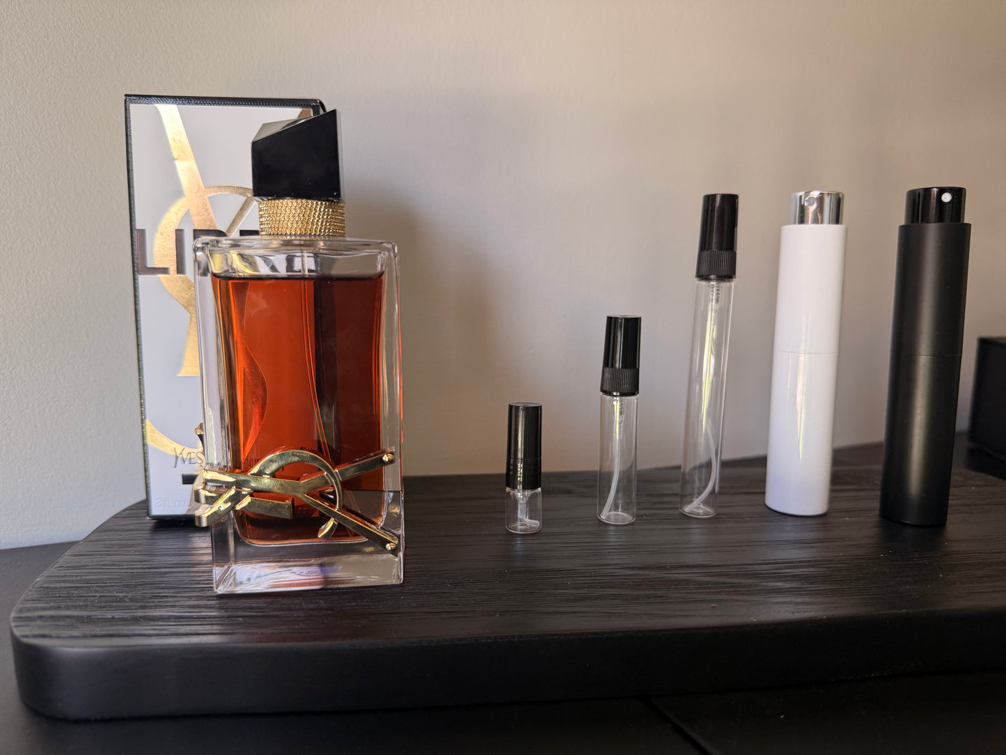 Perfume bottle with packaging and multiple smaller perfume bottles on a dark surface.