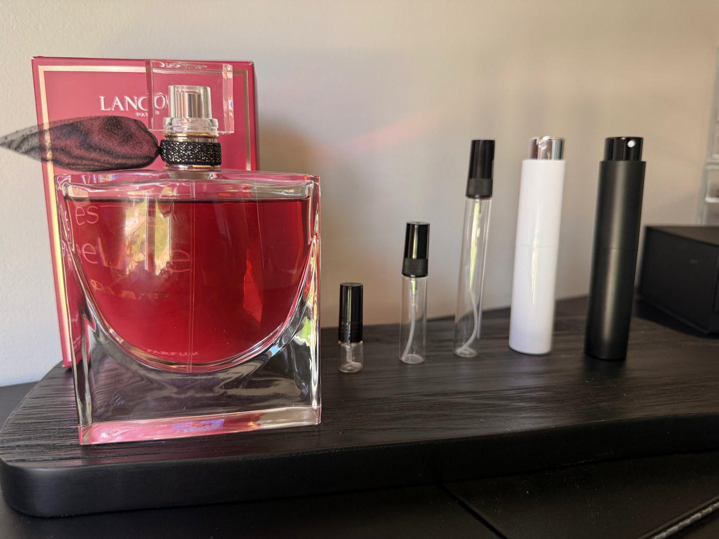 Perfume bottles including a large red bottle and smaller travel-sized bottles on a dark surface.