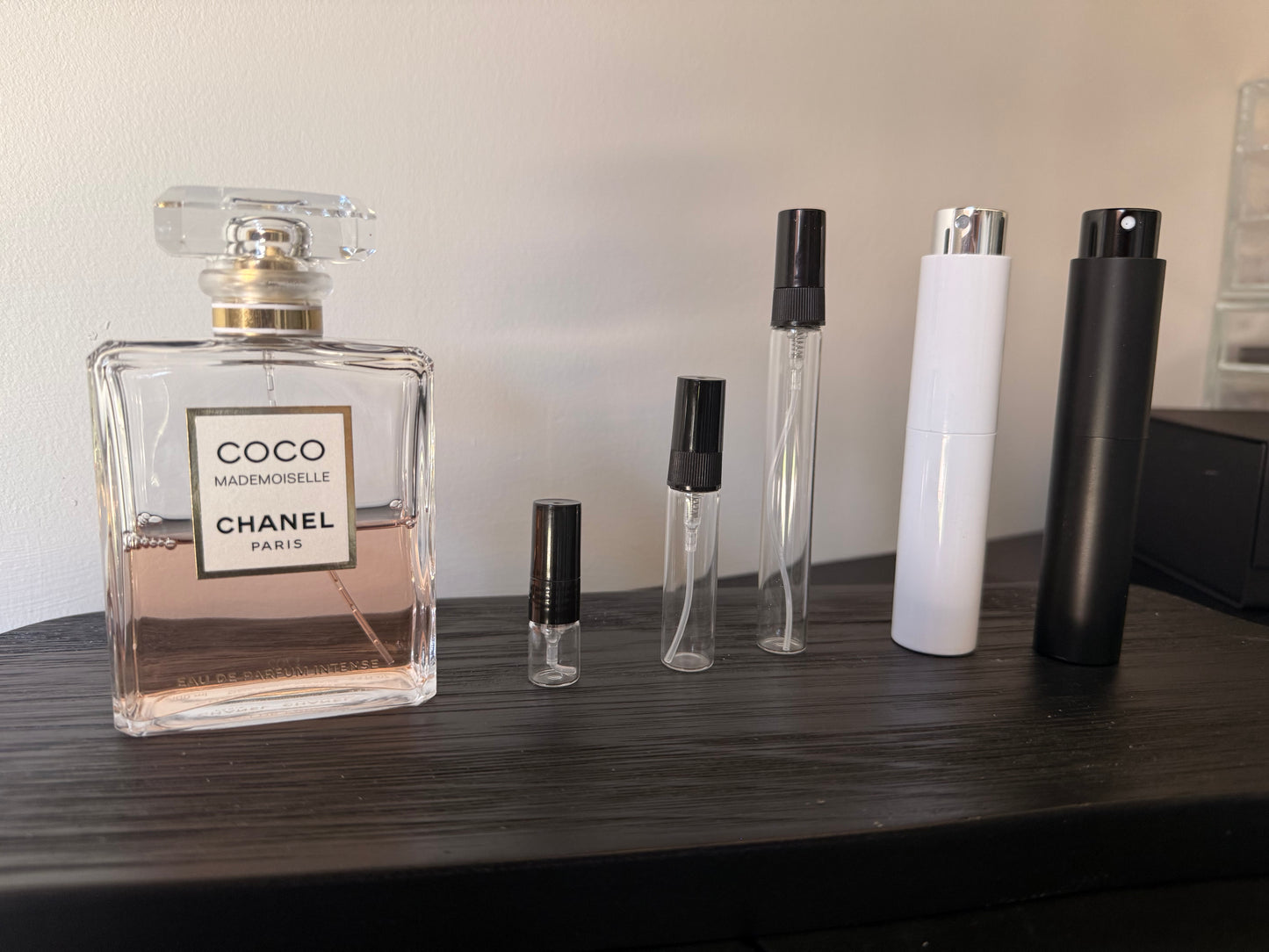 Chanel perfume bottle and smaller travel-sized bottles on a wooden surface.