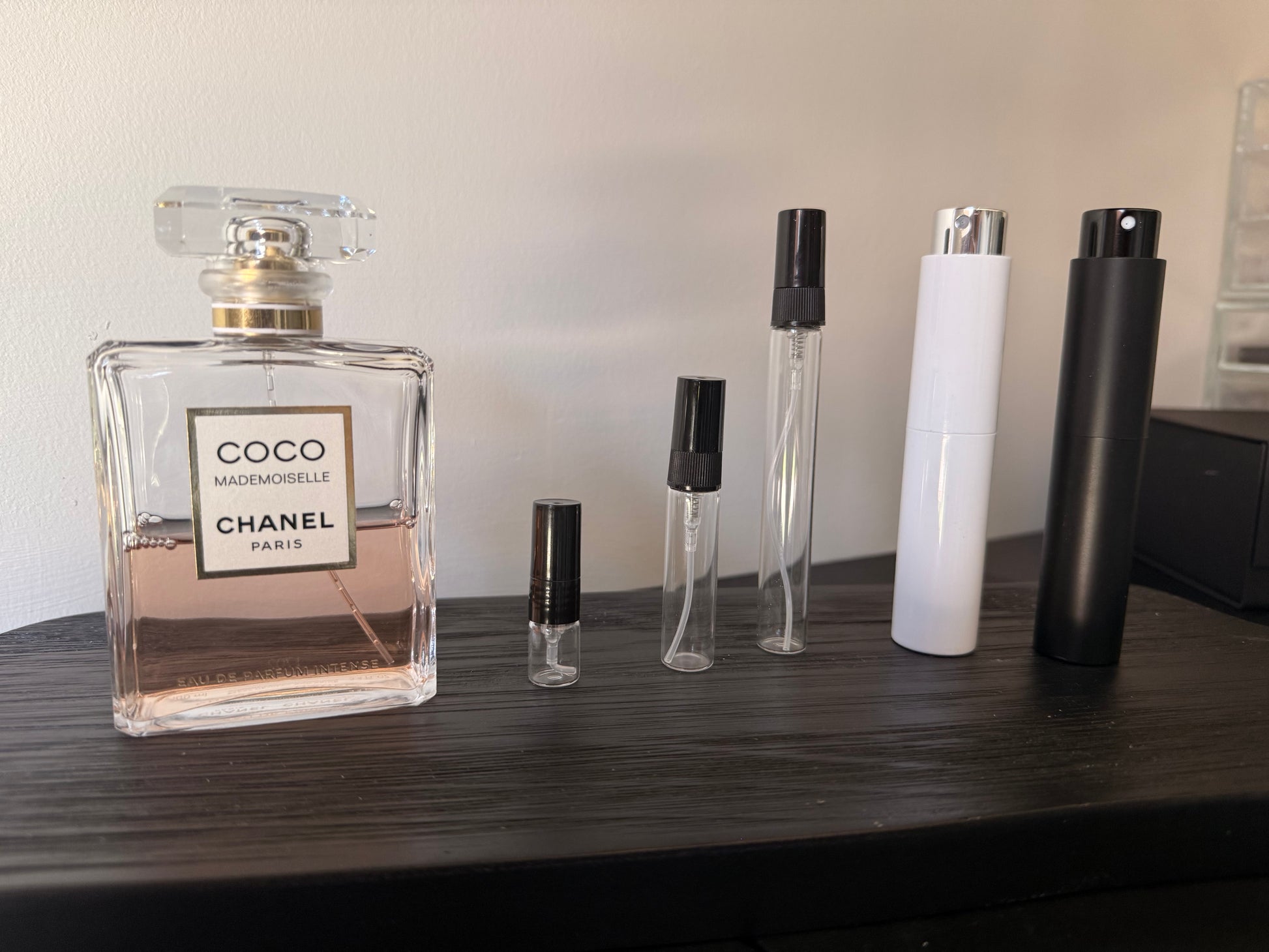 Chanel perfume bottle and smaller travel-sized bottles on a wooden surface.