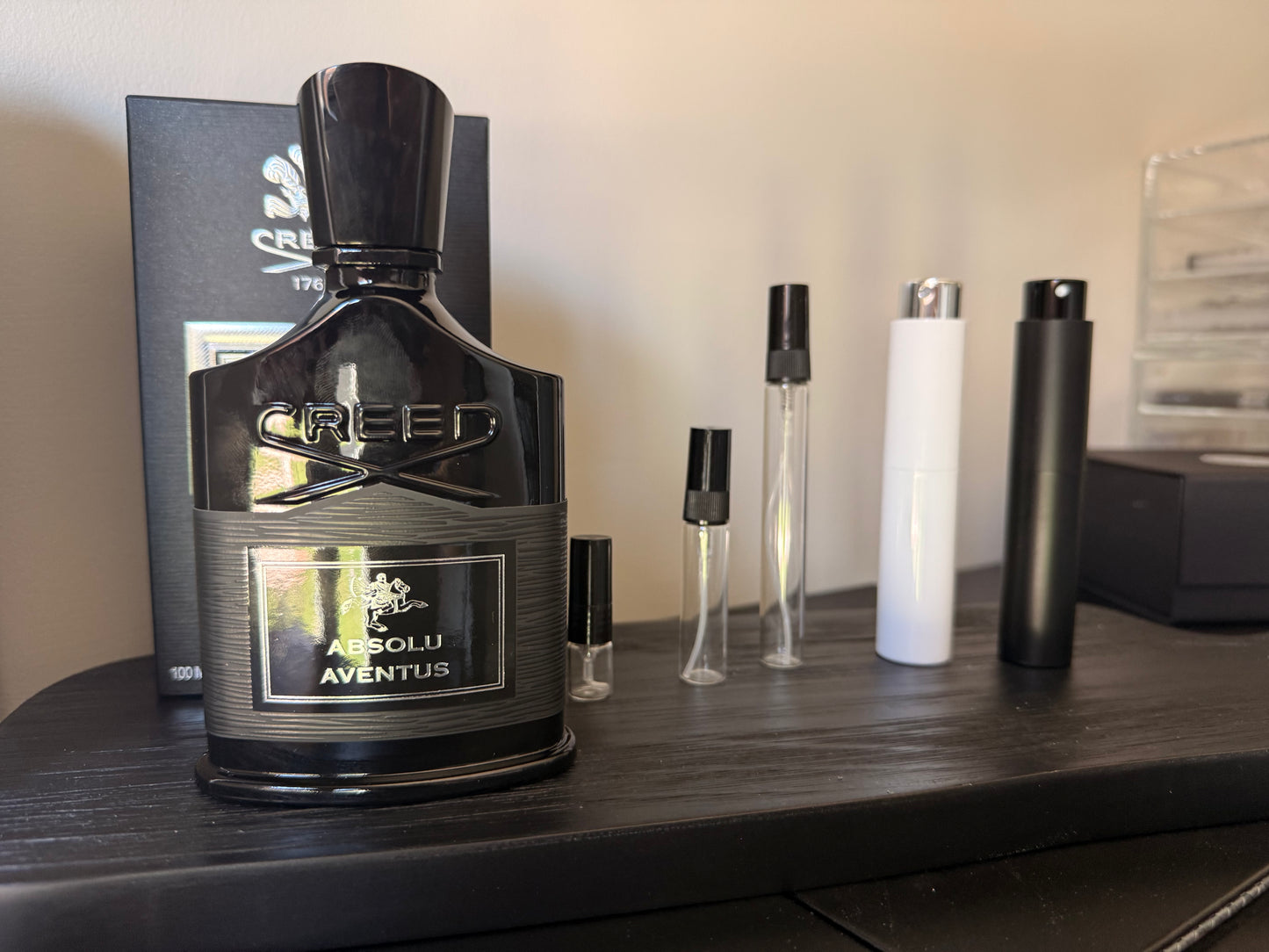 Creed Absolu Aventus perfume bottle on a wooden surface with smaller bottles in the background.