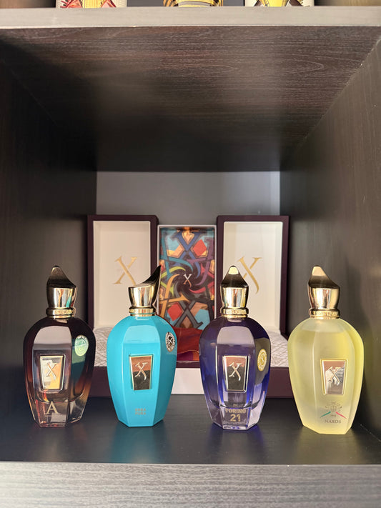 Four perfume bottles on a shelf with framed artwork in the background