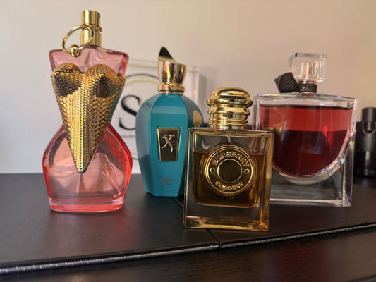 Four perfume bottles of different designs and colors on a reflective surface.