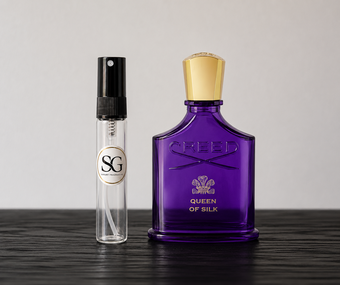 Purple Creed perfume bottle and smaller clear bottle on a dark surface with a light gray background