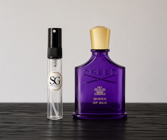 Purple Creed perfume bottle and smaller clear bottle on a dark surface with a light gray background