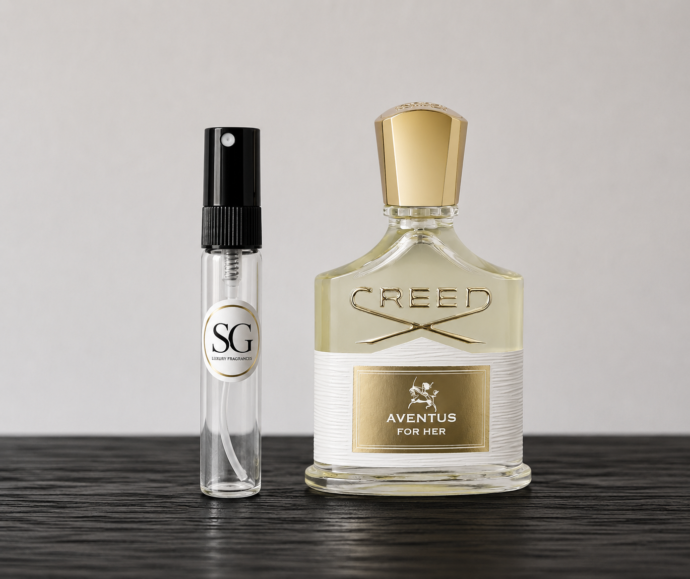 Creed Aventus for Her perfume bottle and a smaller spray bottle on a wooden surface with a light gray background.