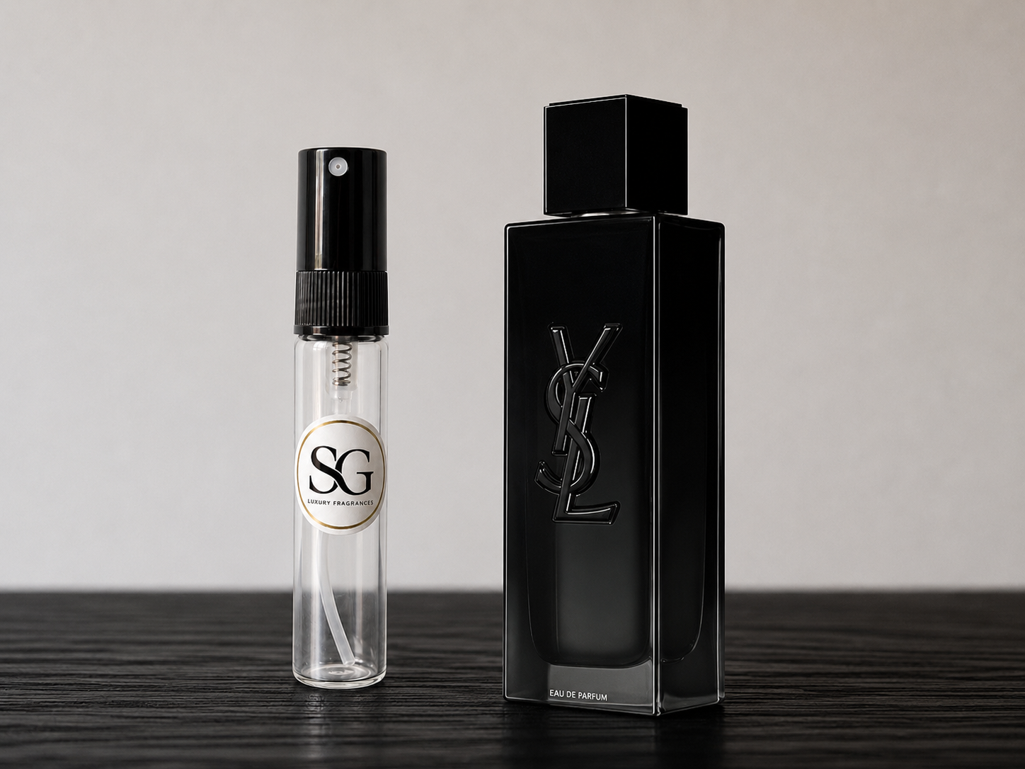 Black perfume bottle and smaller spray bottle on a wooden surface with a neutral background