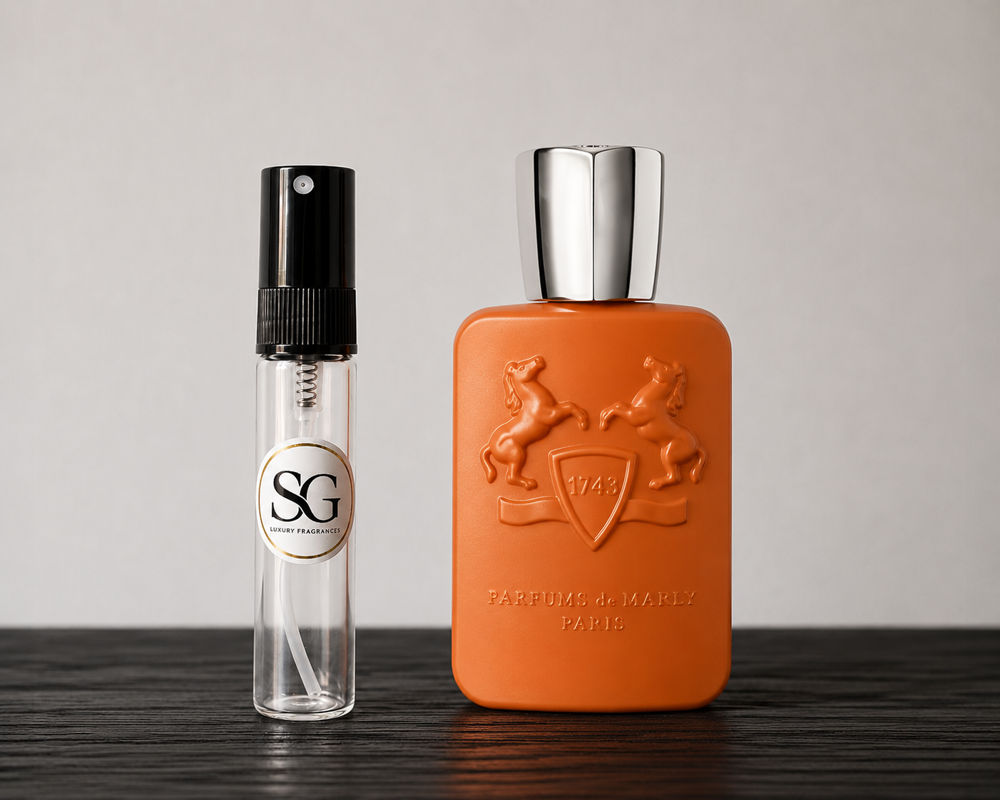 Orange perfume bottle with silver cap and smaller clear bottle with black cap on a wooden surface.