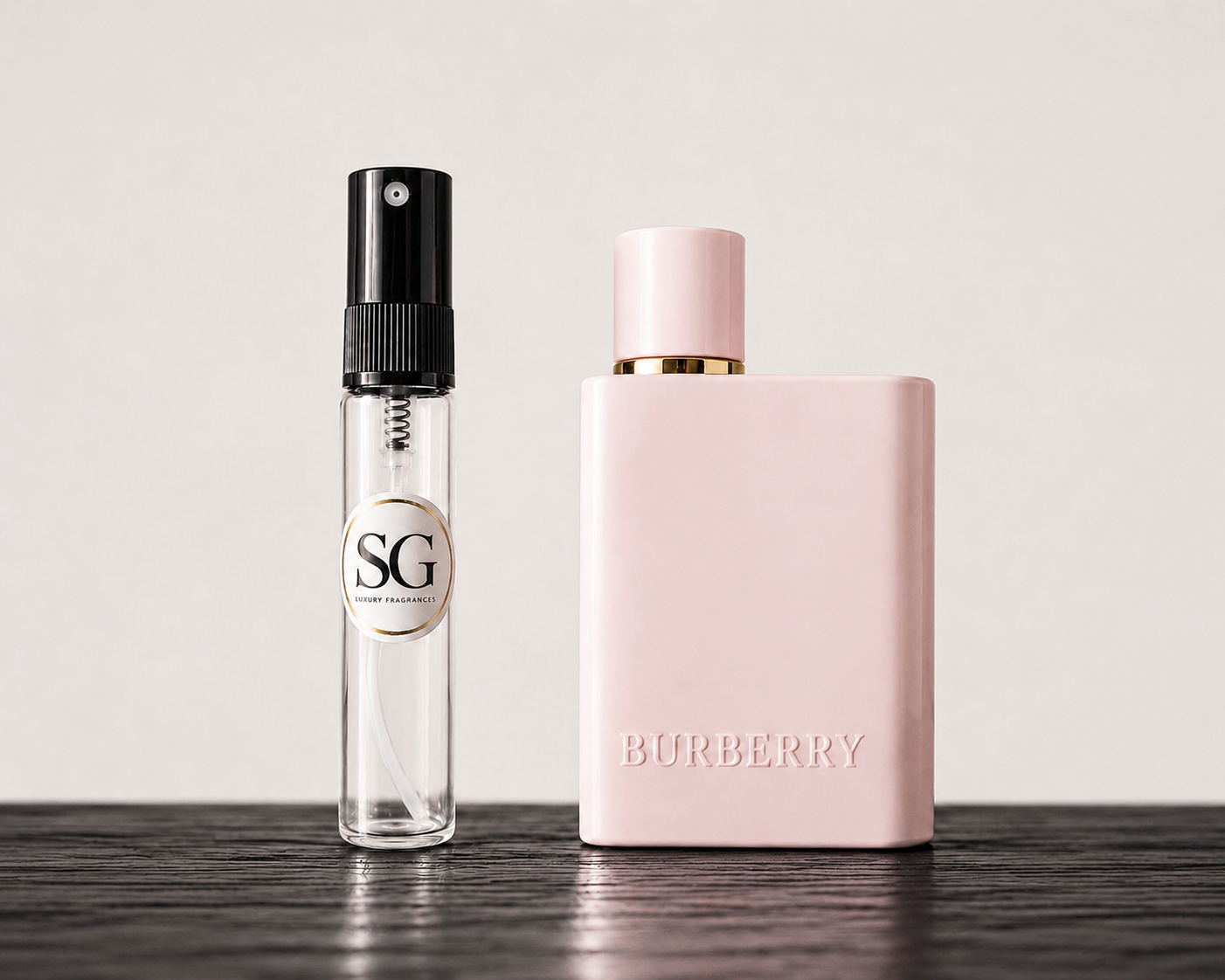 Two perfume bottles, one small and clear with black cap, the other large pink with gold cap, on a wooden surface.