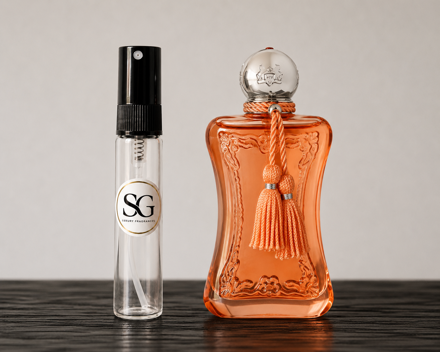 Two perfume bottles, one small and clear with a black spray top and the other large and orange with a decorative cap, on a wooden surface.