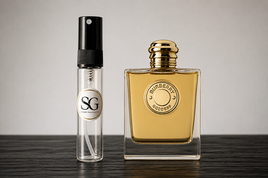 Two perfume bottles, one small and clear with a black spray top, and the other larger and gold, on a wooden surface.