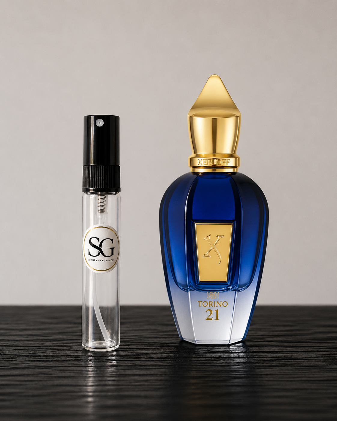 Two perfume bottles, one small and clear with a black cap, and the other large with a gold cap and blue body, on a dark surface.