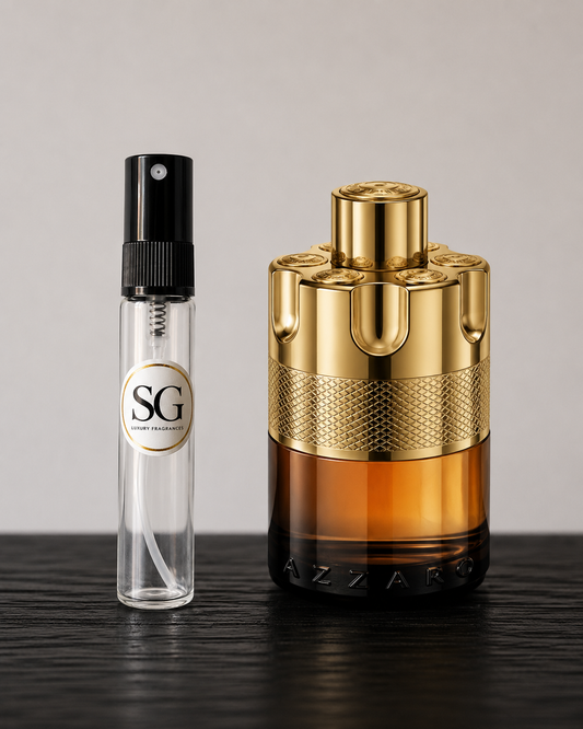 Gold and black perfume bottle with a smaller clear bottle labeled 'SG' on a dark surface.